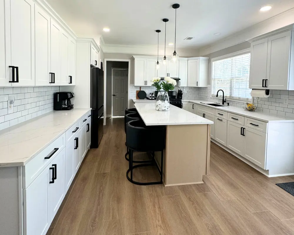 A fully remodeled modern kitchen featuring bright white shaker cabinets, black hardware, a new center island with white quartz countertops, and a white subway tile backsplash by Center Cabinet.